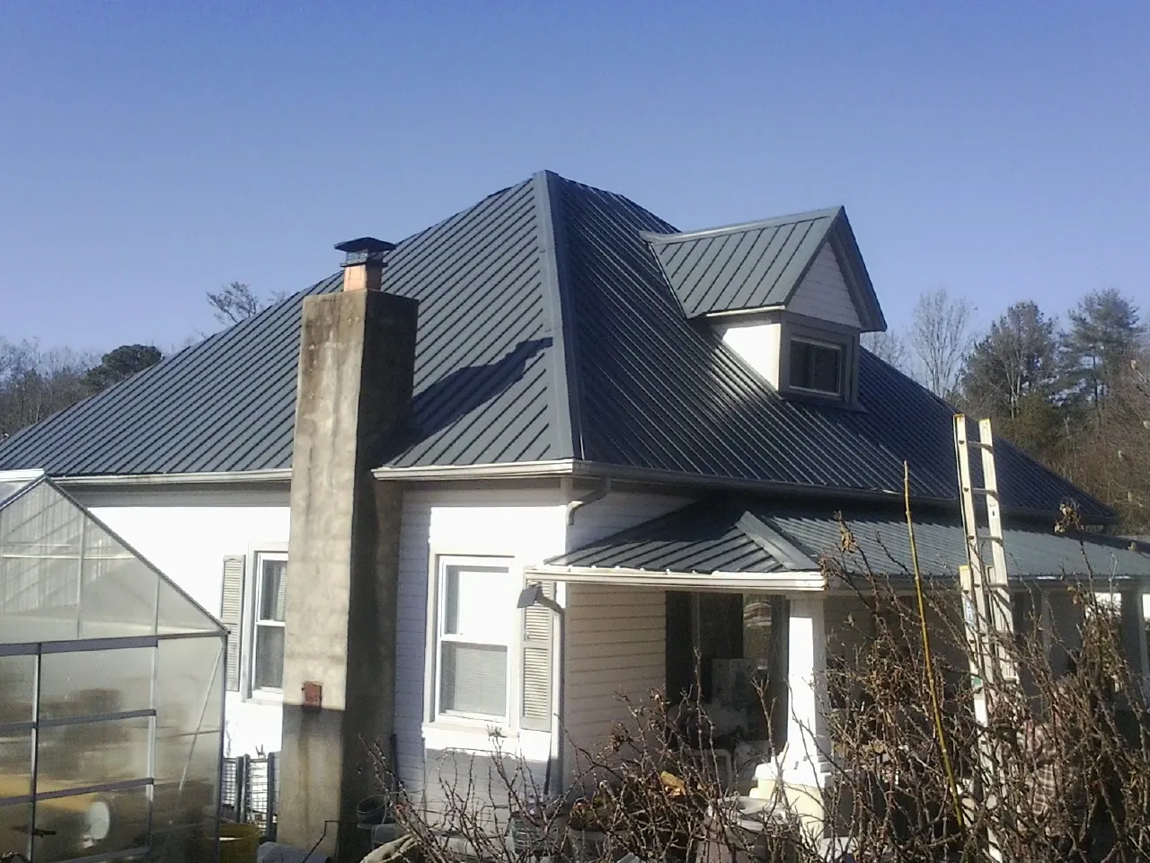 Dark blue standing seam metal roof on a white farmhouse with dormer — Slate & Tile Roof Repair by Roofing Brothers in Donnelly