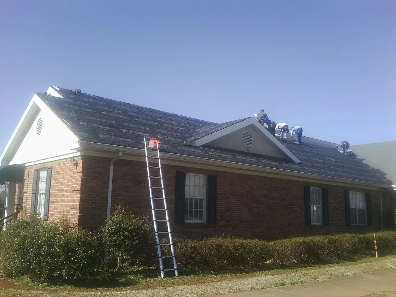 Crew tearing shingles off a brick ranch roof with a ladder set — Metal Roof Repair work by our crew in Donnelly