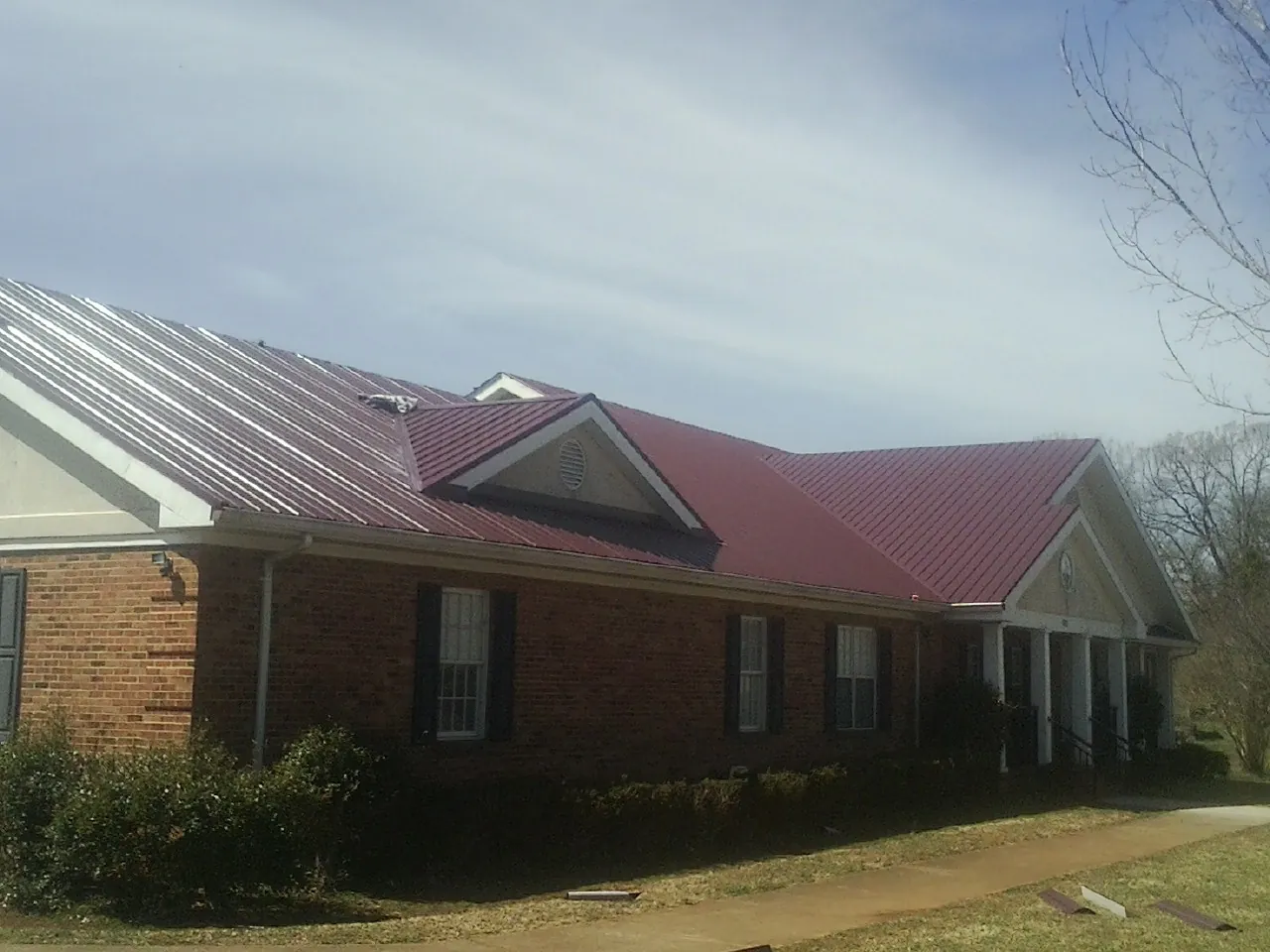Red metal roof with gabled entries on a long brick building, from a Hail Damage Roof Repair job in Donnelly