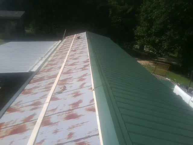 Old rusted panels beside newly installed green metal roofing — Wind Damage Roof Repair by Roofing Brothers in Donnelly