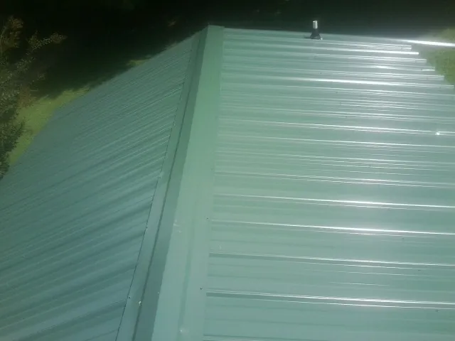 New green metal panels meeting at the ridge of a roof — Flat Roof Repair work by our crew in Donnelly