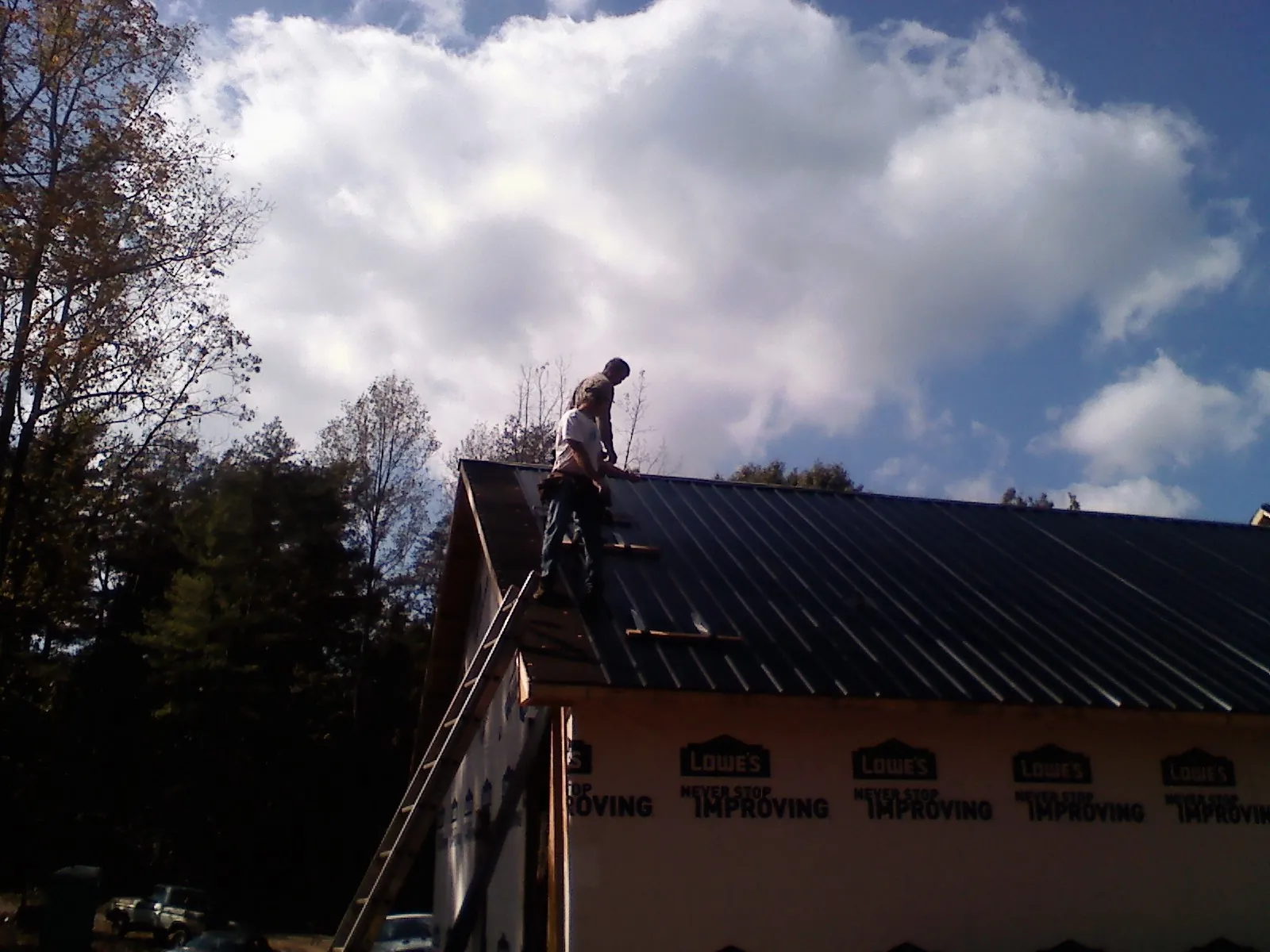 Roofer fastening dark metal panels high against a cloudy sky, from a Roof Inspection job in Donnelly