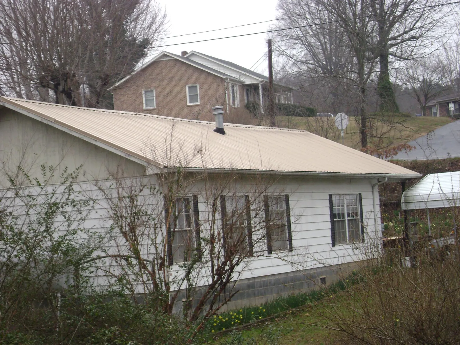 Tan metal roof on a white sided house set into a hillside — Commercial Roofing by Roofing Brothers in Donnelly