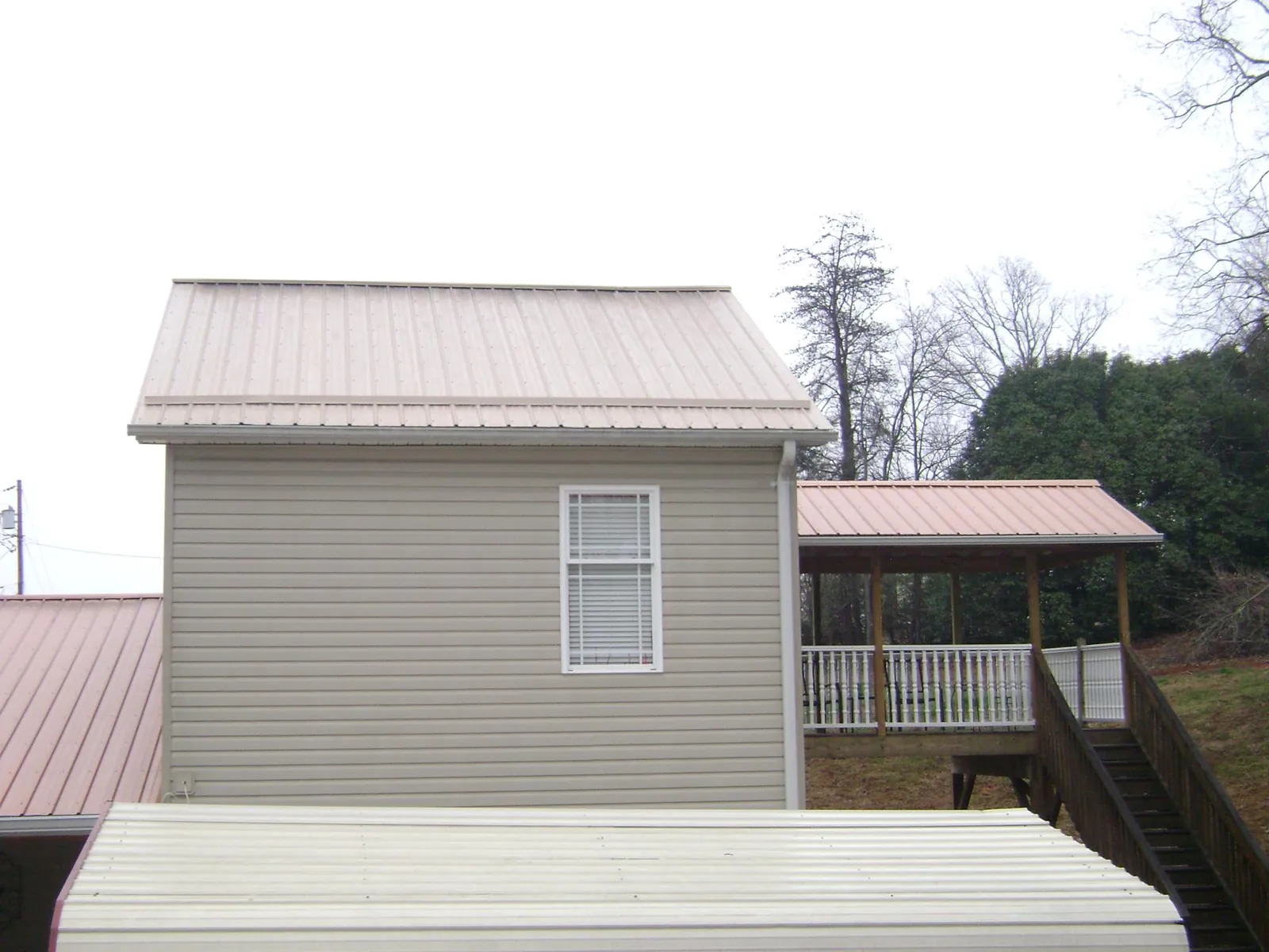 Tan metal roofs on a two story addition and attached porch, from a Roof Replacement job in Donnelly